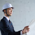 設計図を見ながら現場を監督するスーツ姿の男性