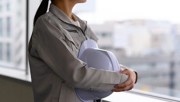 建物の中から遠くを見る作業着姿の女性