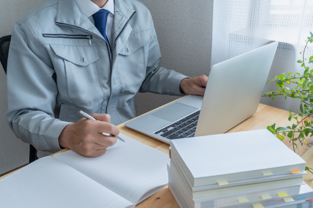 パソコンを使った作業をする作業着の男性