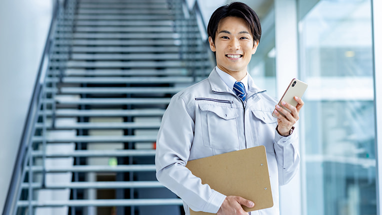 笑顔でスマホとバインダーを持つ作業着姿の男性施工管理