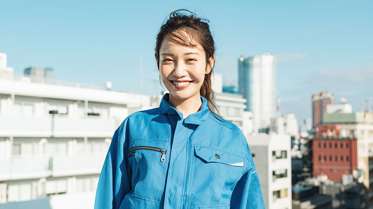 青空の下でさわやかな笑顔を浮かべる作業着姿の女性