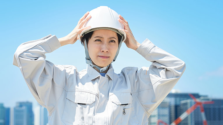 青空の下でヘルメットをかぶって気合いを入れる作業着姿の女性施工管理