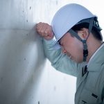 しんどそうな表情で壁にもたれかかる作業着姿の男性施工管理