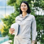 ビルの前でヘルメットを持って笑顔で立つ作業着姿の女性施工管理