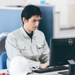 事務所でパソコン作業を行う作業着姿の男性施工管理